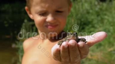 小<strong>男孩</strong>手里拿着一只<strong>青蛙</strong>在河边的海滩上。 慢动作